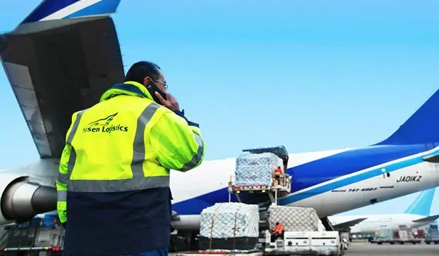 Yusen Logistics employee on the phone with cargo being loaded onto an airplane behind them